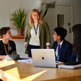 The Head of Sixth Form stands talking with 4 seated students who are studying in the study area. They look relaxed and happy.